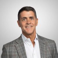 A professional headshot of Carl Eschenbach, the Chief Executive Officer of Workday, a smiling white man wearing a white shirt and a gray plaid blazer.